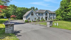 A large, light blue house with a driveway leading to the entrance, surrounded by lush greenery and trees. - Spacious 7-bedroom country house in perfect Kingston retreat (Kingston)
