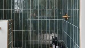 Een douche met een handdouche, een houten plank met flessen en een betegelde vloer.