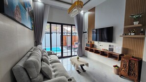 Un salon moderne avec un canapé gris, un téléviseur et une piscine visible à travers les portes vitrées.