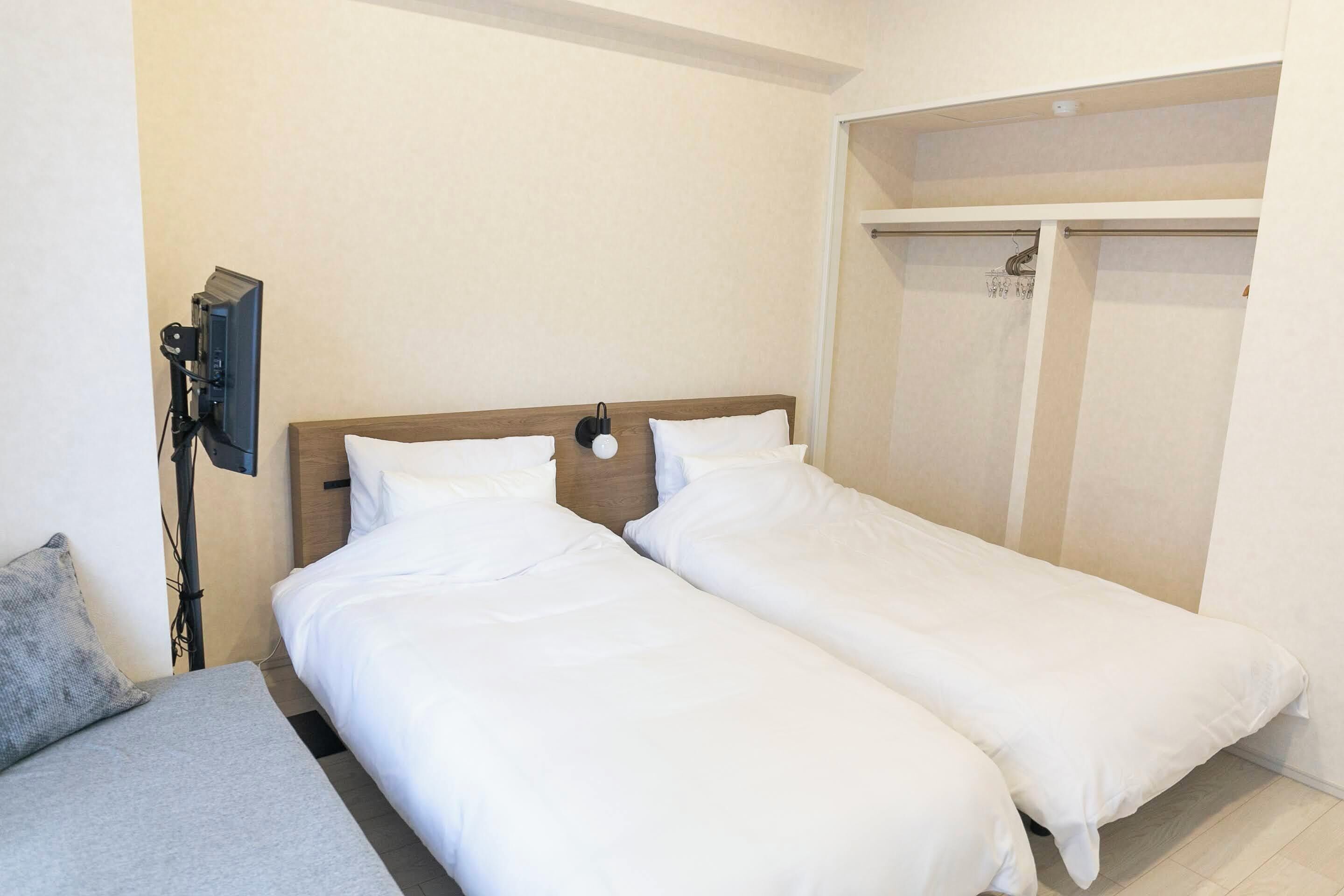 A hotel room with two single beds, a grey sofa, a TV, and a wardrobe.