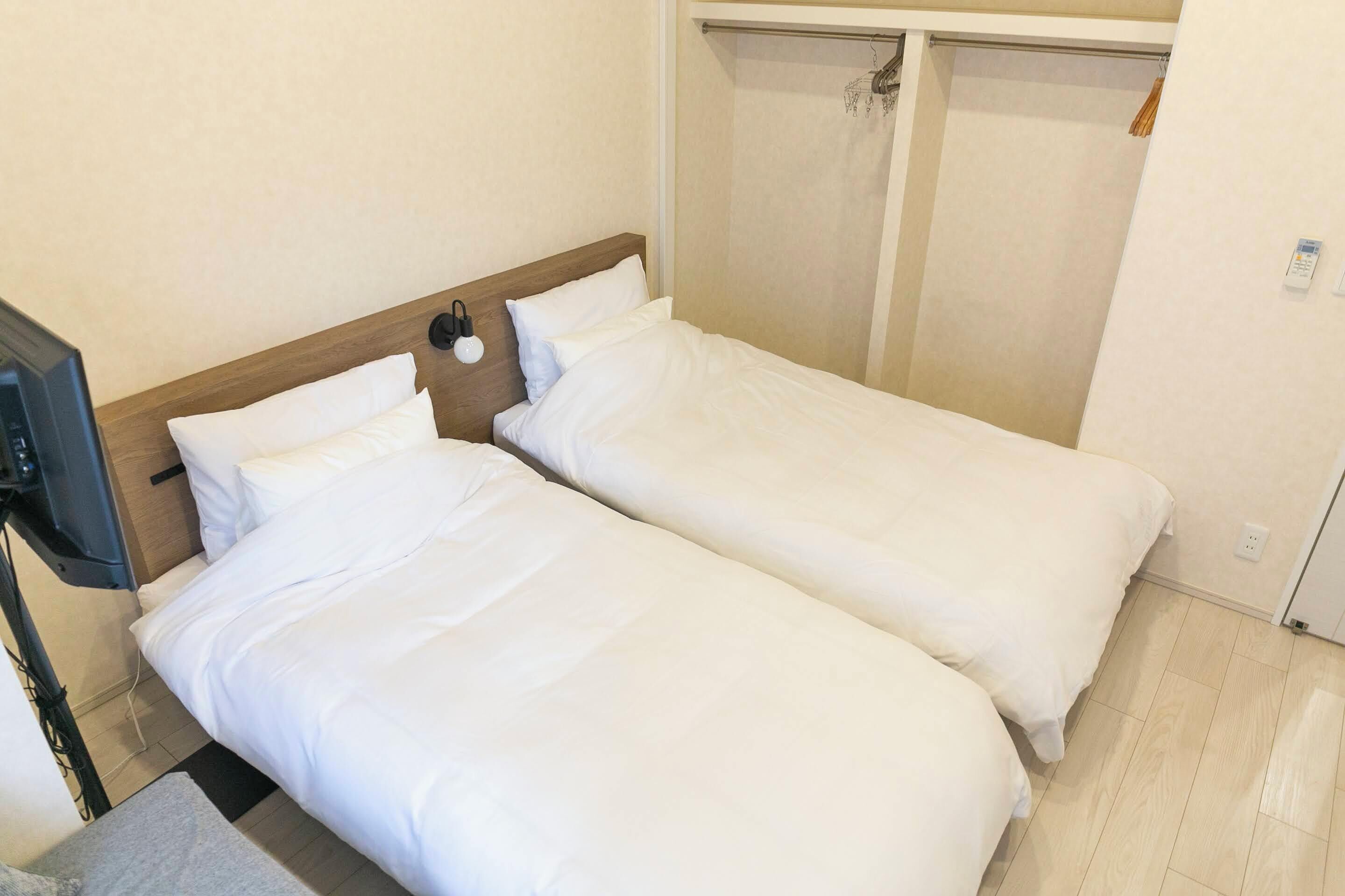 Habitación de hotel con dos camas individuales, un cabecero de madera, una mesita de noche y un televisor.