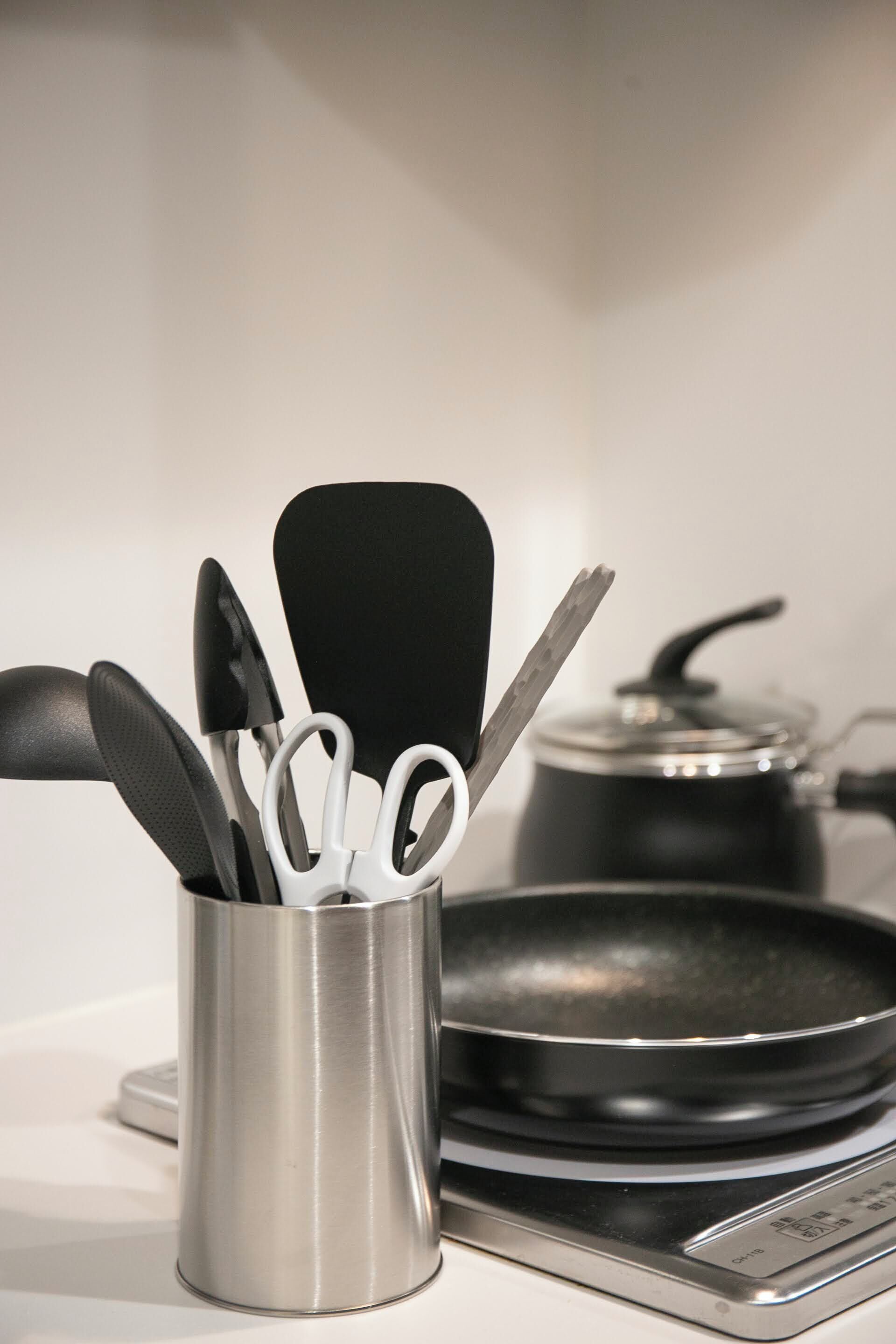 Eine Küche mit einem Edelstahl-Utensilienhalter, der einen Pfannenwender, ein Messer und eine Schere enthält. Eine Bratpfanne steht auf dem Herd, ebenso ein Kochtopf.