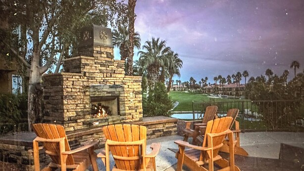 Un área de estar al aire libre con sillas Adirondack y una chimenea de piedra.