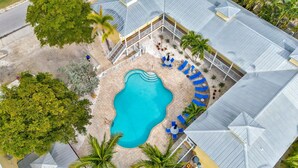 En vy från ovan av ett semesterområde med en swimmingpool omgiven av solstolar och ett överbyggt område med en trappa som leder upp till en terrass.