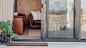 Une entrée moderne avec une porte coulissante en verre, un lambris en bois et un espace détente comprenant deux canapés en cuir et des coussins.