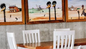 Un coin repas avec une table en bois et des chaises blanches, un canapé en cuir marron et trois tableaux encadrés accrochés au mur.