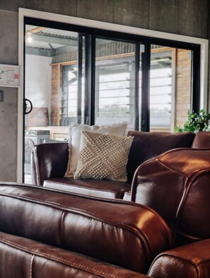 Ein Ledersofa mit einem gewebten Kissen in einem Raum mit großen Fenstern und Blick auf ein Industriegebiet.