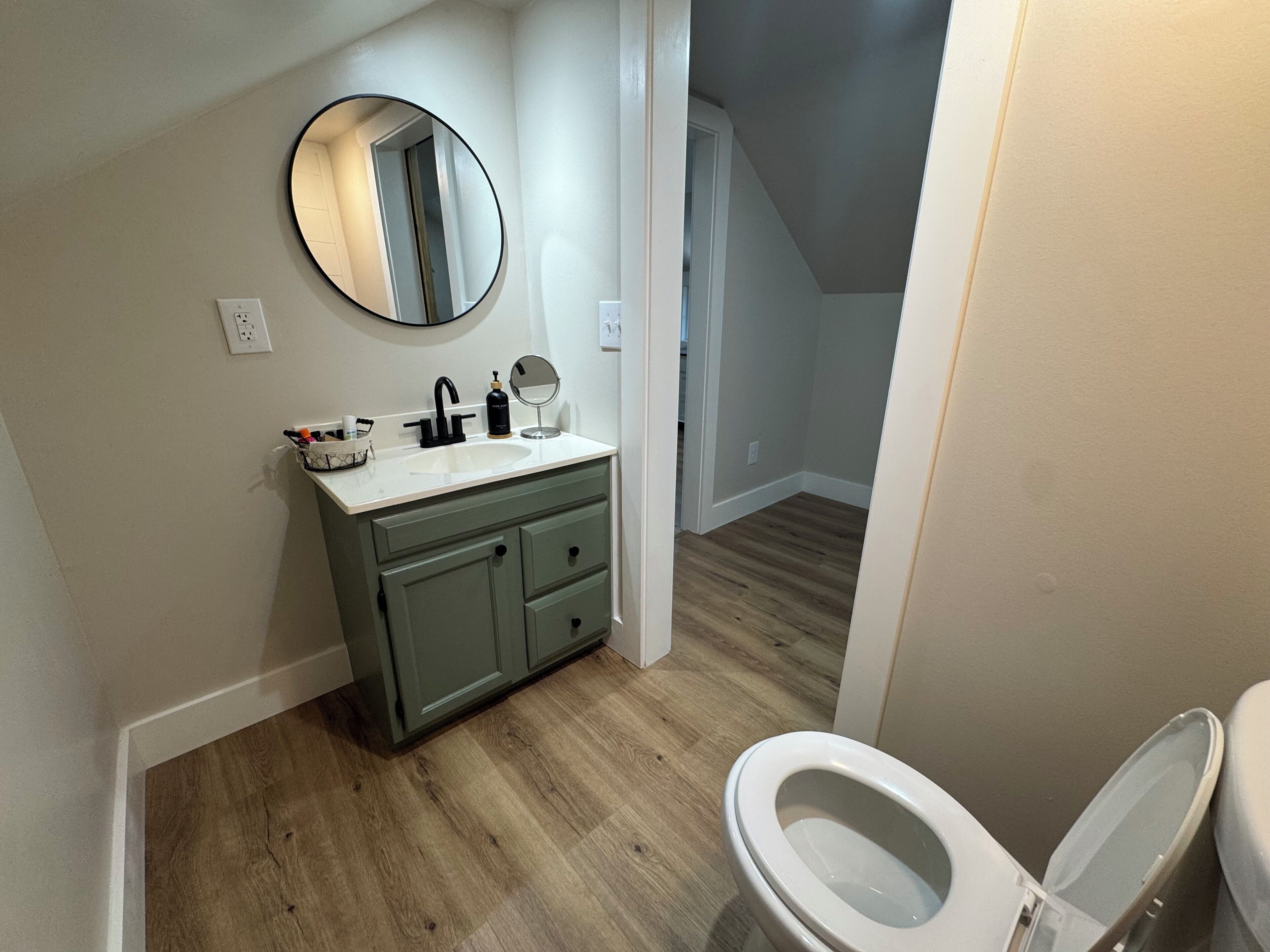 A bathroom with a wooden floor, a white sink with a mirror above it, and a toilet.