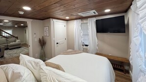 A bedroom with a wooden ceiling, a bed with white bedding, a bench, a TV mounted on the wall, and a staircase leading to another room. - Relaxing Farmhouse in beautiful Butler (Butler)
