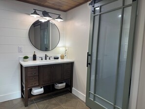 A modern bathroom with a round mirror, dual sinks, dark wooden cabinets, and a glass shower enclosure. - Relaxing Farmhouse in beautiful Butler (Butler)