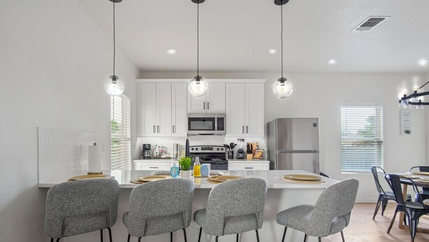 Une cuisine moderne avec des meubles blancs, un îlot central doté de tabourets et des luminaires suspendus.