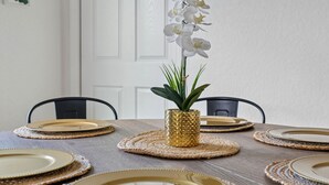 Une table à manger avec des assiettes à bord doré, un set de table en fibres tressées et une orchidée en pot.