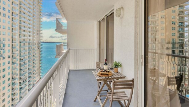 Ein Balkon mit Tisch für zwei Personen, mit Blick auf ein Gewässer und hohe Gebäude.