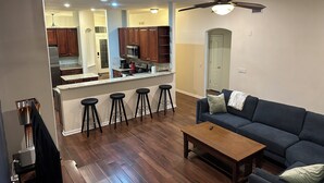 Una sala de estar con un sofá azul oscuro, una mesa de centro de madera y una zona de bar con taburetes.