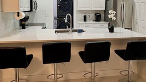 A modern kitchen with white cabinets, a central island with bar stools, a built-in washer and dryer, and a refrigerator. - Spacious Home in lovely Lehigh Acres (Lehigh Acres)
