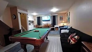 Una mesa de billar, un sofá y una televisión en una sala de estar.