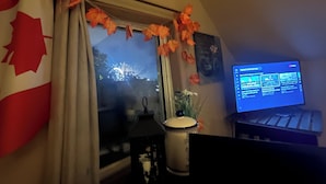 Una habitación con ventana decorada con hojas otoñales, una bandera canadiense y un monitor de computadora que muestra un sitio web de noticias.