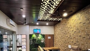 A reception area with a wooden desk, a television, and a wall with a brick pattern. - Hotel Leela Vilas- A Boutique Hotel (Pushkar)