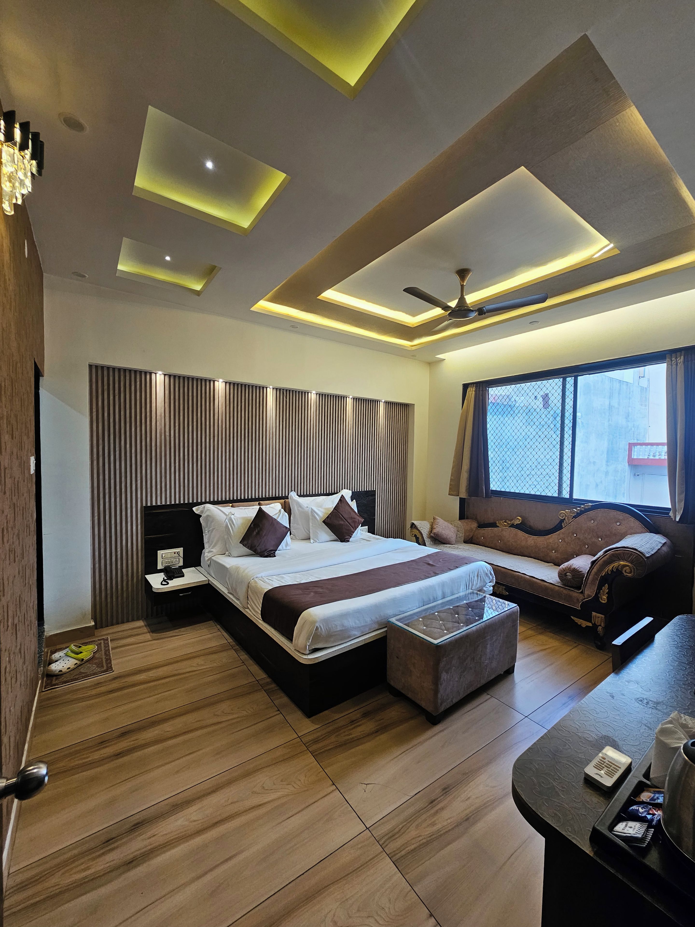 A modern bedroom with a large bed, a sofa, a desk, and a ceiling fan.