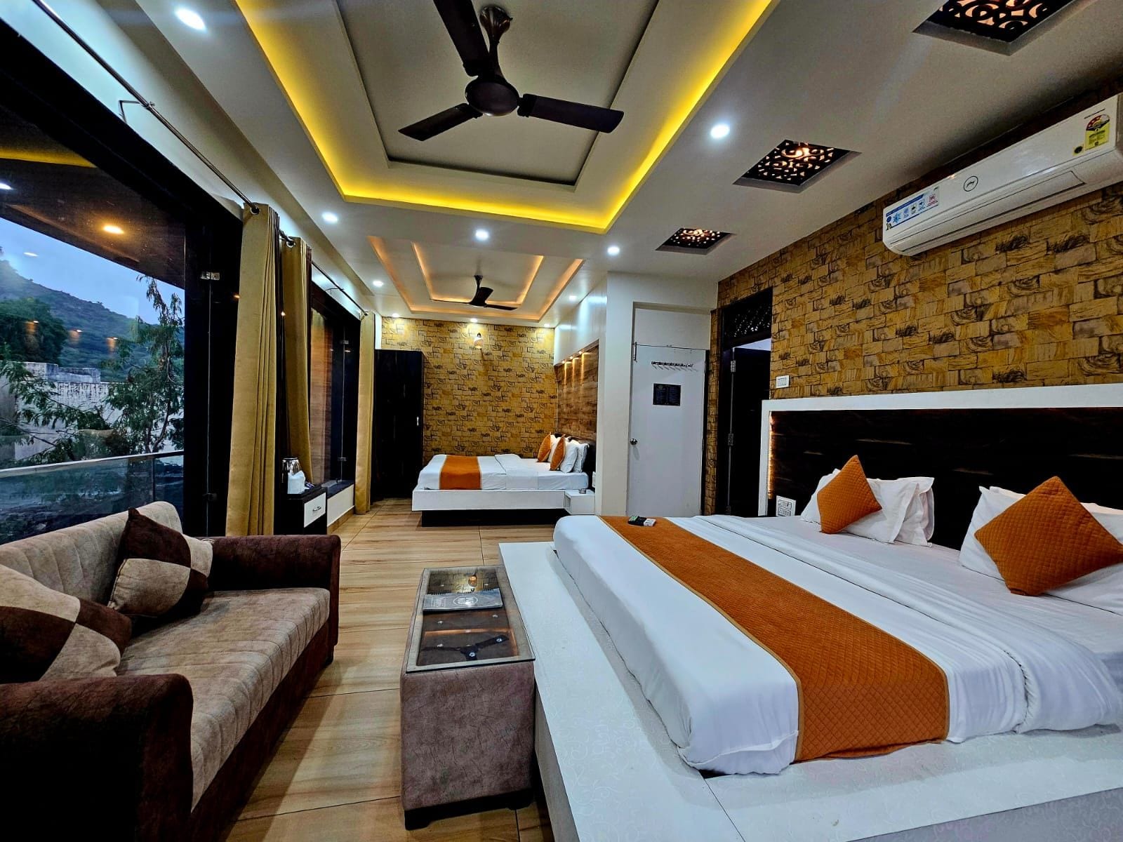 A hotel room with two beds, a sofa, a coffee table, and a view of the outdoors.