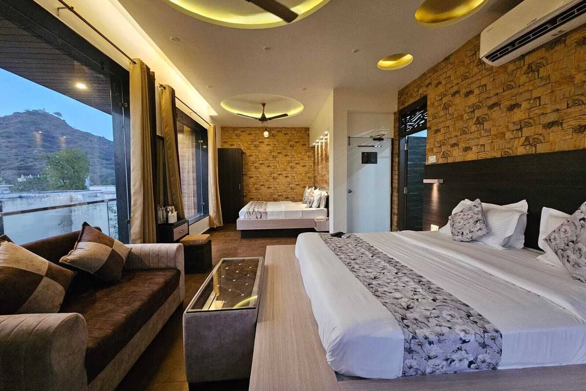 A hotel room with a large bed, a sofa, a small table, and a view of the outdoors.