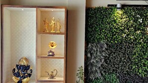 A room with a wooden cabinet displaying religious statues, a wall-mounted green plant, and a potted plant. - Hotel Leela Vilas- A Boutique Hotel (Pushkar)