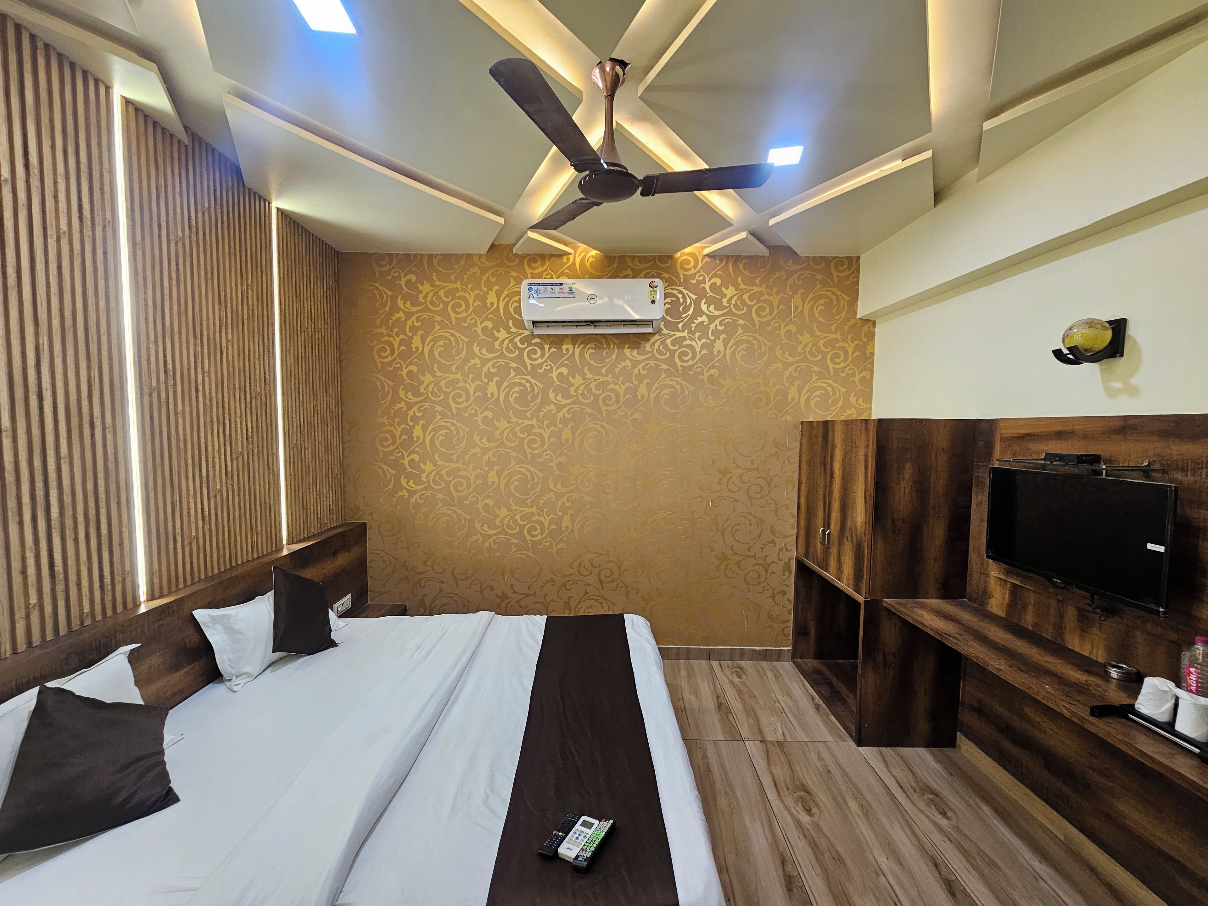 Una camera d'albergo con un letto, una ventola a soffitto, un condizionatore, una TV e un armadio in legno.