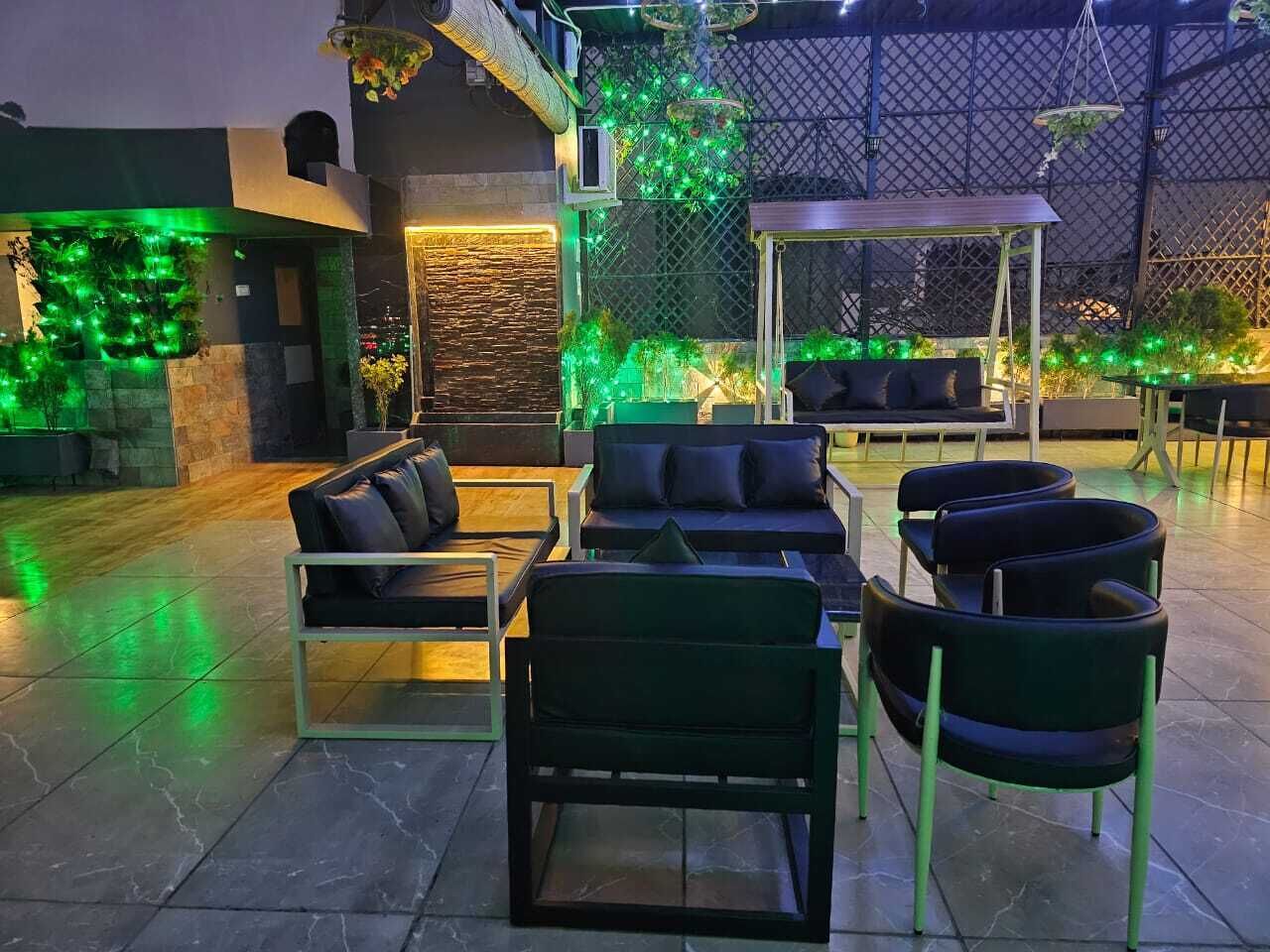 Un espacio al aire libre con sillones, sillas y mesas, rodeado por un muro decorativo con luces verdes.