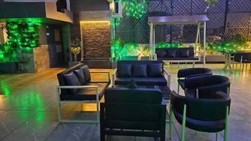 Un espacio al aire libre con sillones, sillas y mesas, rodeado por un muro decorativo con luces verdes.