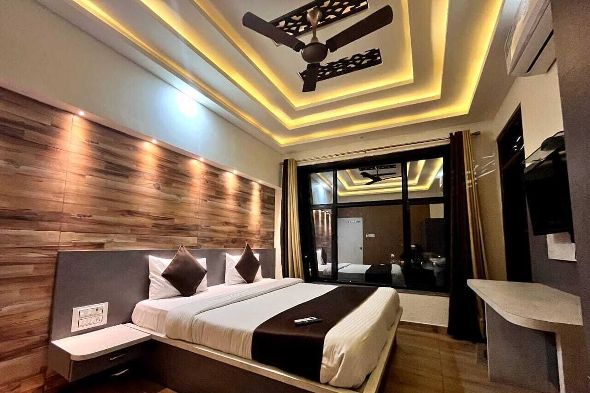 A modern hotel room with a large bed, a bedside table, a ceiling fan, and a large window.