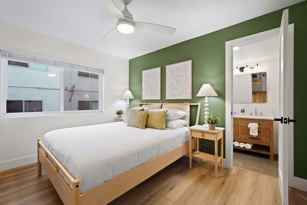 A bedroom with a bed, bedside tables, a ceiling fan, a window, and a bathroom visible through an open door. - Explore South Park from 2-Story Home Sleeps 8 (San Diego)