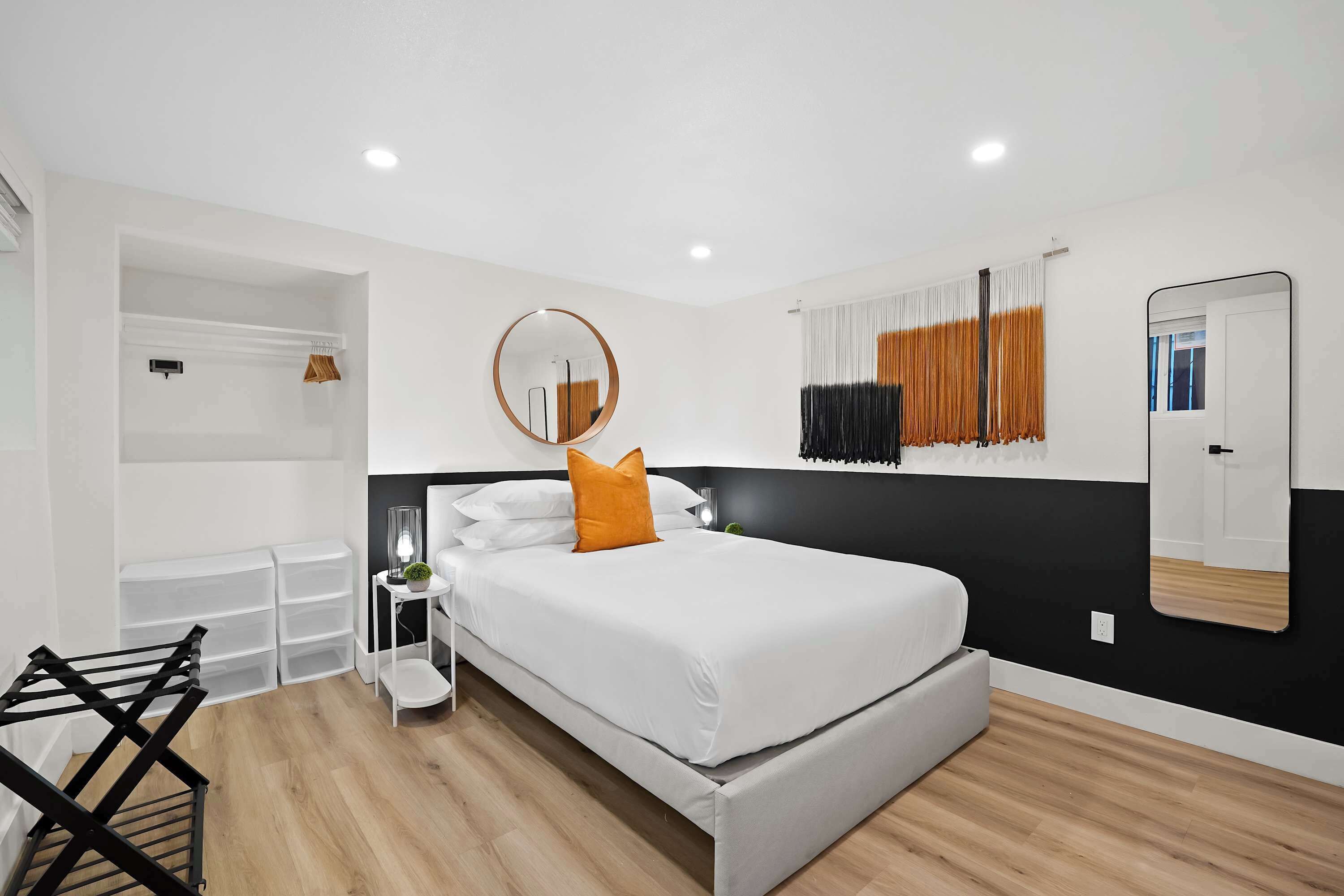 A bedroom with a bed, a round mirror, a wardrobe, and a drying rack.
