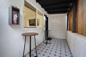 Pequeña zona de balcón cerrada, con suelo de baldosas, dos mesas, un extintor y una ventana.