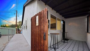 Un pequeño edificio de una sola planta con un portón de madera, una mesa pequeña y suelo de baldosas.