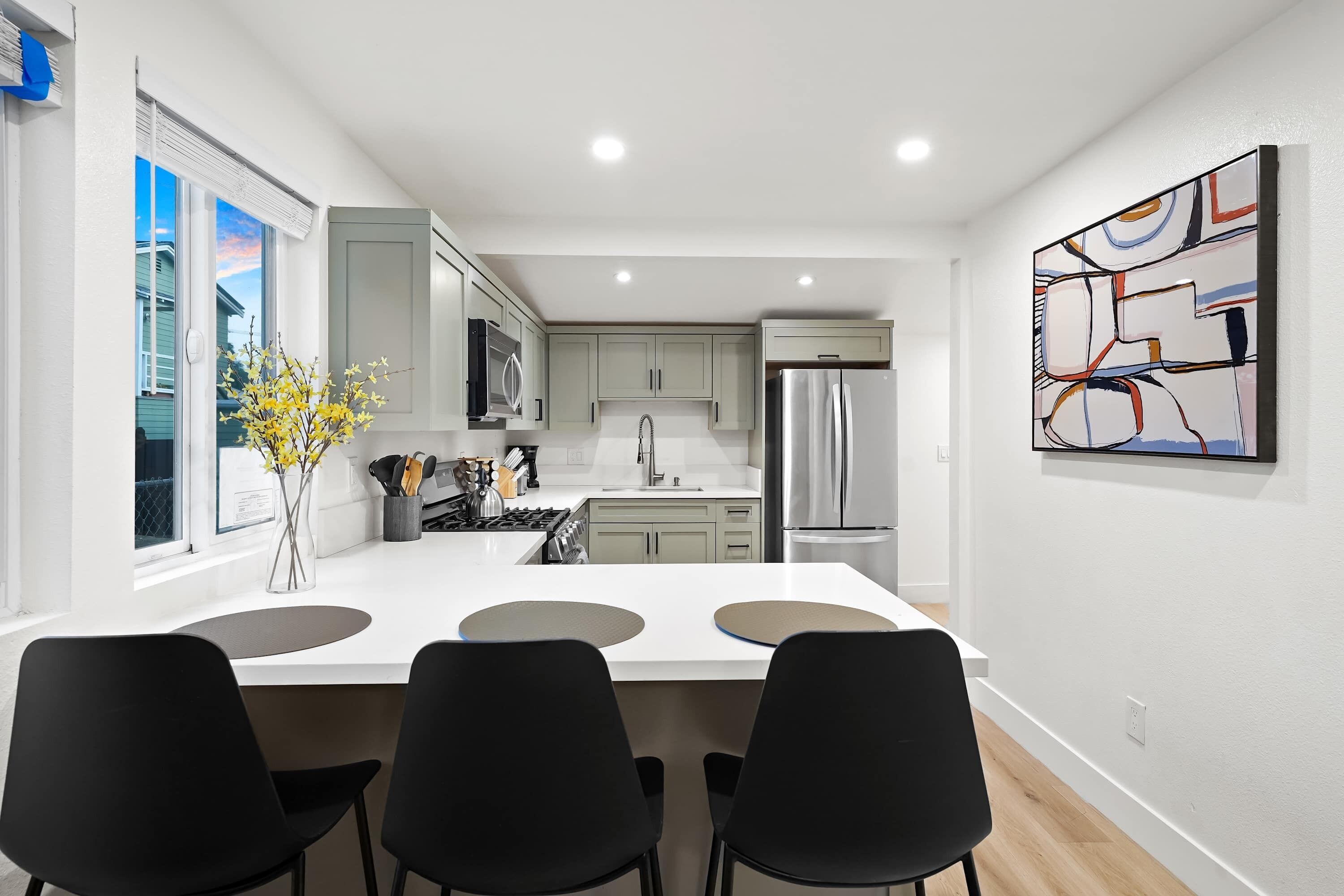 Una cocina moderna con armarios blancos, un refrigerador de acero inoxidable y un comedor con sillas negras.