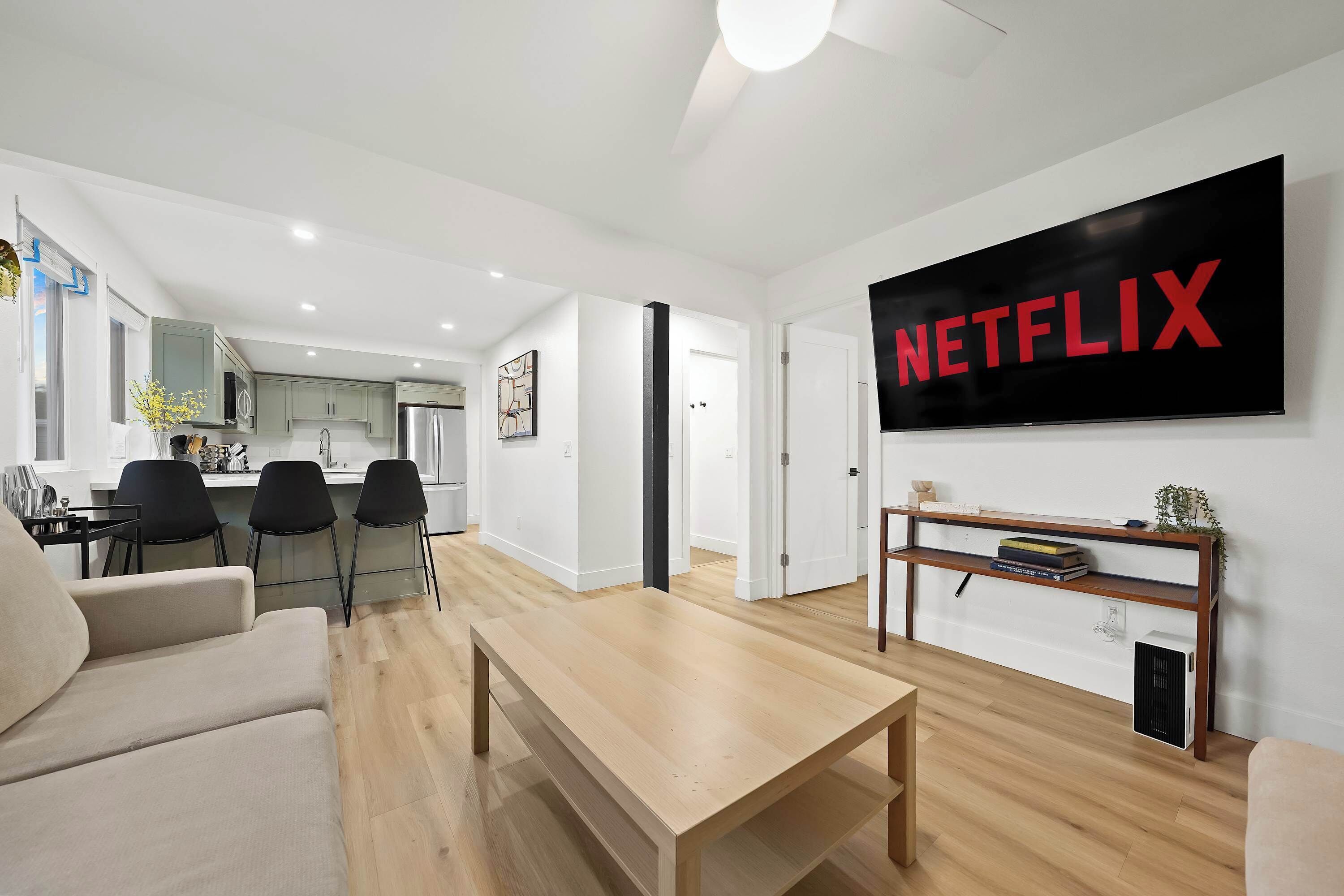 Ein modernes Wohnzimmer mit Couchtisch aus Holz, einem beigefarbenen Sofa und einem Fernseher, der das Netflix-Logo zeigt.