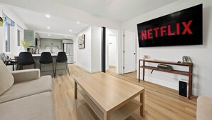 Ein modernes Wohnzimmer mit Couchtisch aus Holz, einem beigefarbenen Sofa und einem Fernseher, der das Netflix-Logo zeigt.