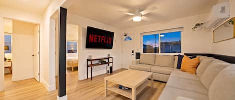Una sala moderna con un sofá, una mesa de centro, un televisor montado en la pared y un ventilador de techo.