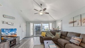 A spacious living room with a large sofa, a television, a ceiling fan, and a view through the glass doors. - 3 Bedroom Condo Near Wildwood Beach & Boardwalk (Wildwood)