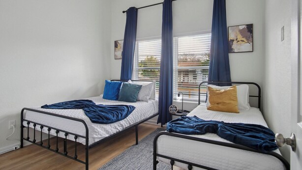 Een slaapkamer met twee eenpersoonsbedden, een raam met zonwering en een klein nachtkastje met een lamp.