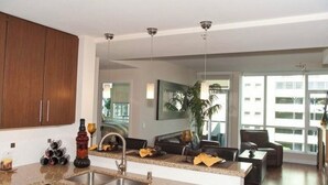 Een moderne keuken met granieten werkbladen, een inbouwspoelbak en houten kastjes. Er is een eethoek met een tafel en stoelen, en een groot raam met uitzicht op de stad.
