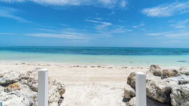 A beach with clear blue water and a sandy shore. There are white rocks in the foreground. - Key Colony Beach oceanview condo, beach + heated pool (Key Colony Beach)