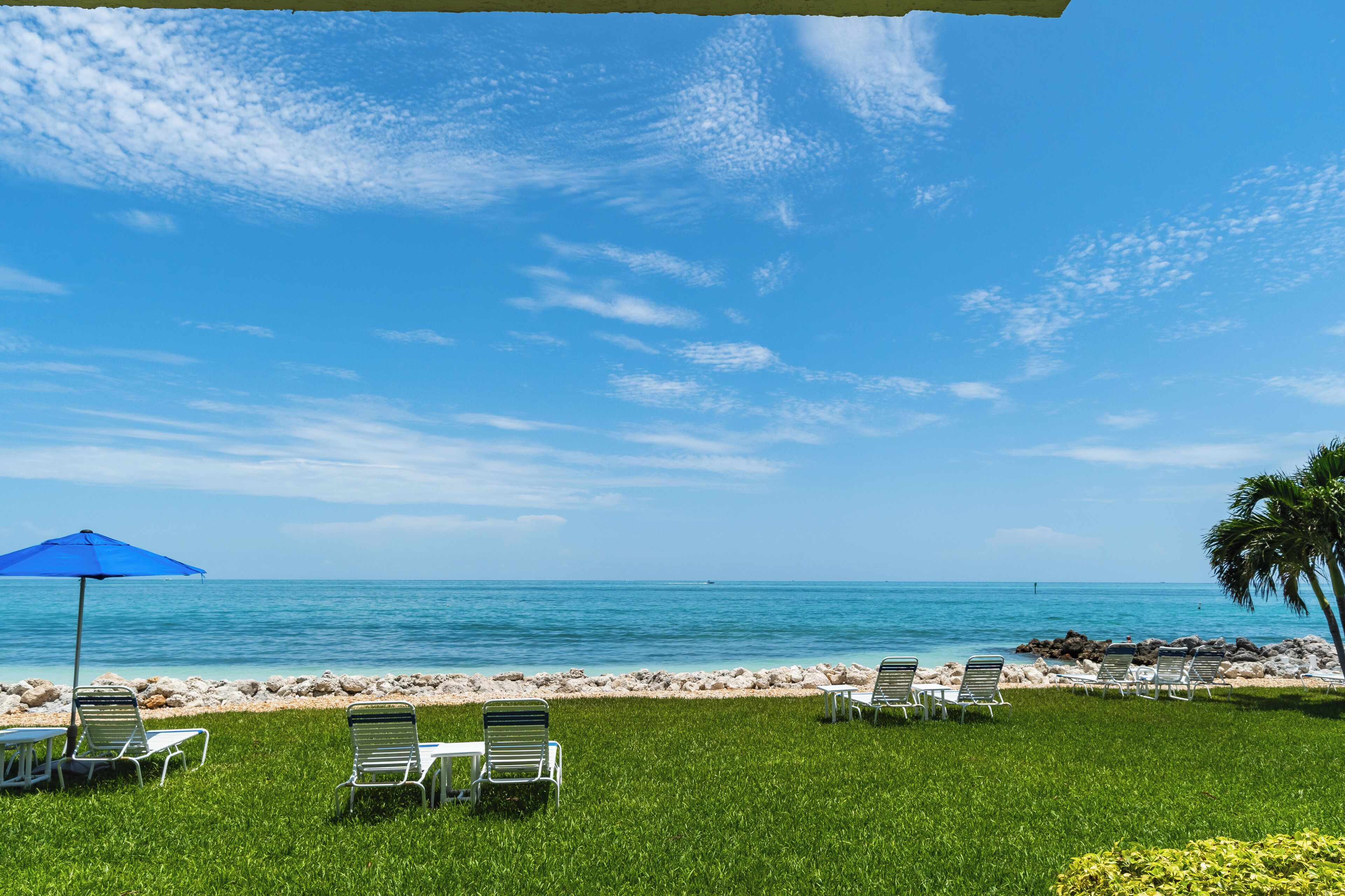 A beachside view with lounge chairs and a blue umbrella, overlooking the ocean.