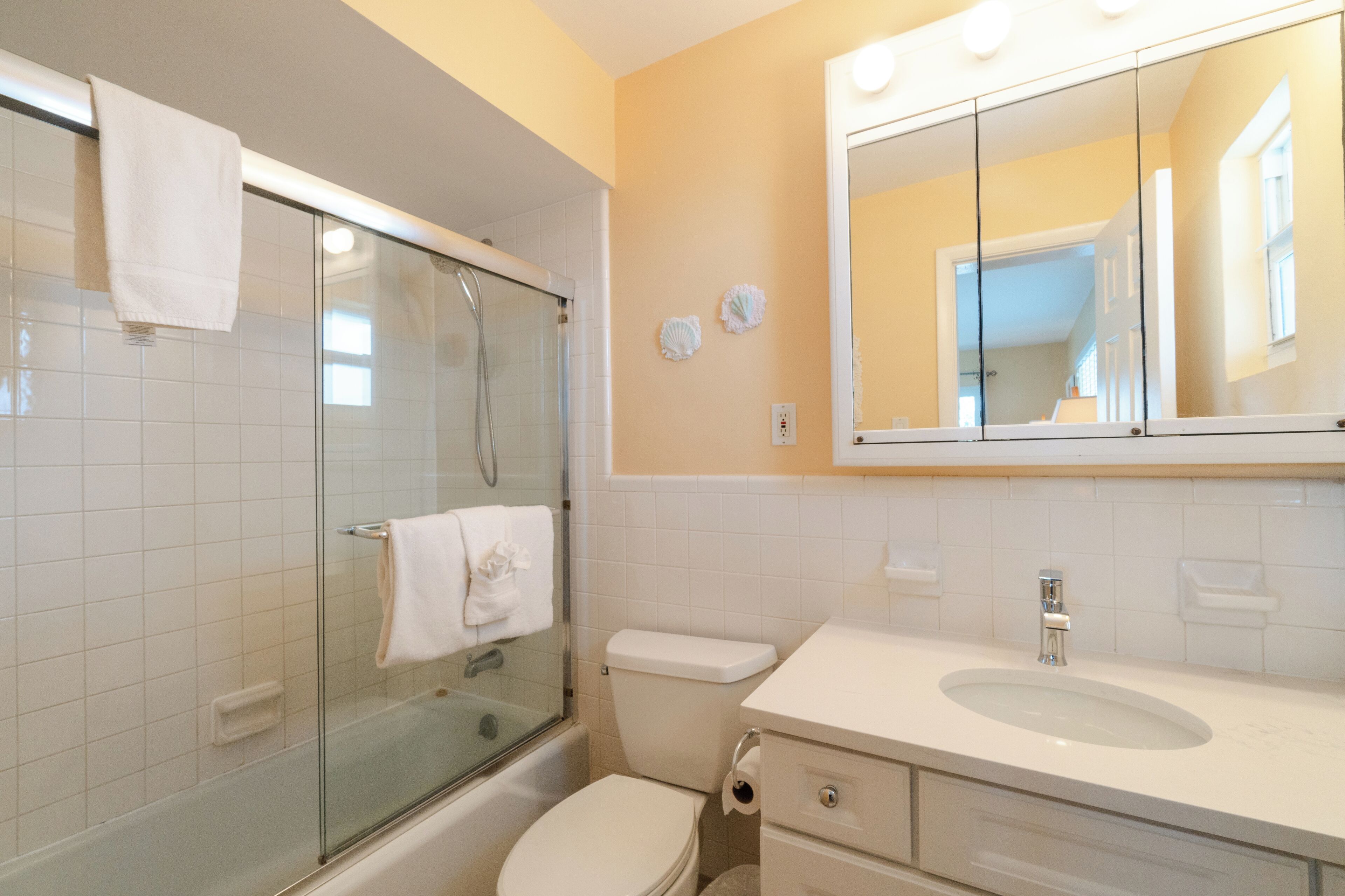 A bathroom with a glass-enclosed shower, a white toilet, a sink with a mirror above it, and a towel hanging on the shower door.