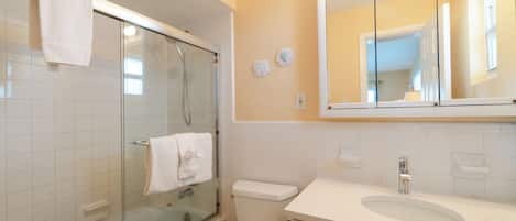 A bathroom with a glass-enclosed shower, a white toilet, a sink with a mirror above it, and a towel hanging on the shower door.