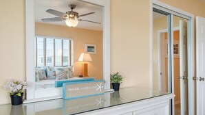 A room with a glass-top vanity, a ceiling fan, a bed with a view to the outside, and a door leading to another room. - Key Colony Beach oceanview condo, beach + heated pool (Key Colony Beach)