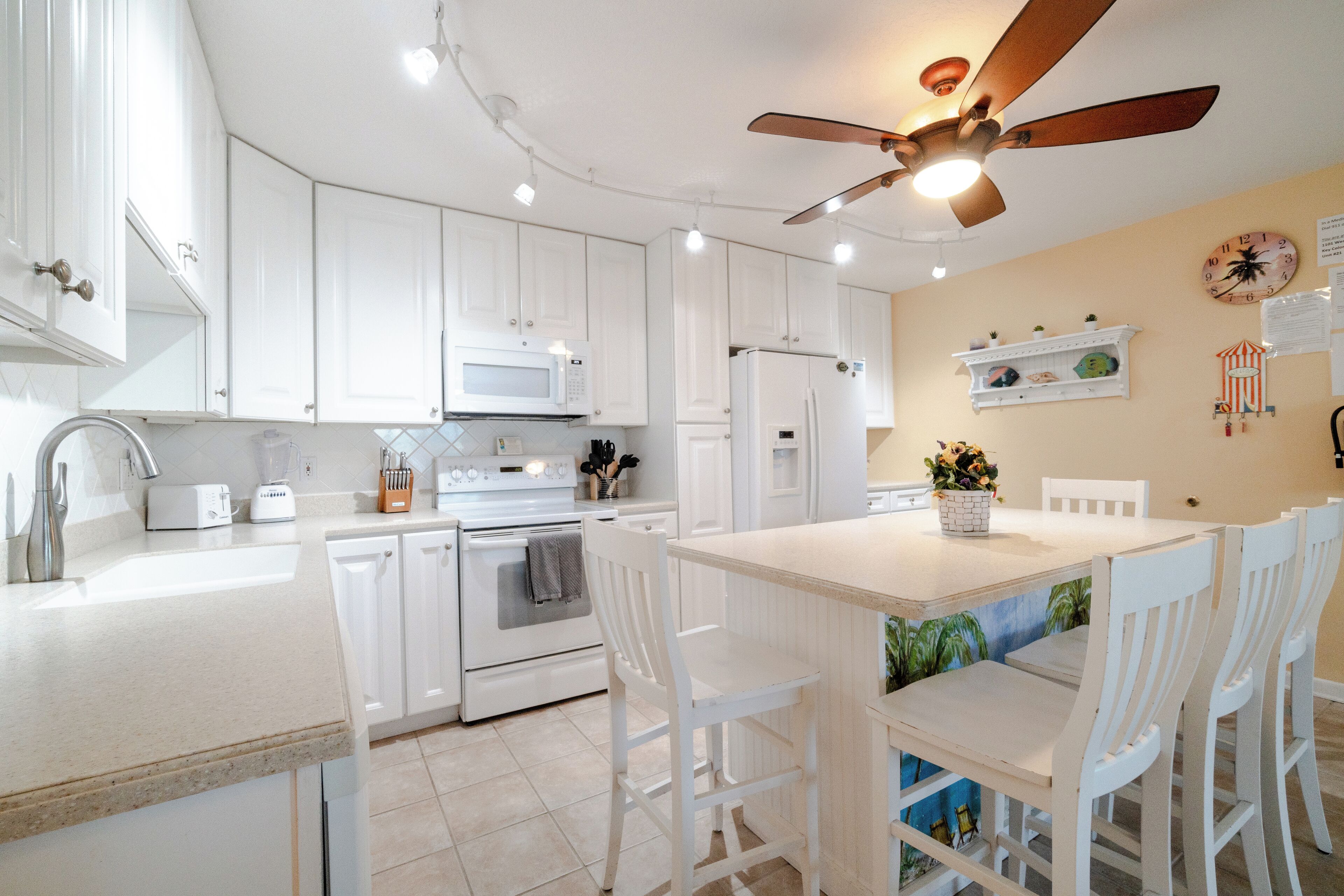 Una cocina moderna con armarios blancos, una isla central con asientos, un ventilador de techo y un microondas.
