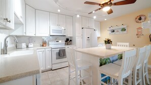 A modern kitchen with white cabinetry, a central island with seating, a ceiling fan, and a microwave. - Key Colony Beach oceanview condo, beach + heated pool (Key Colony Beach)