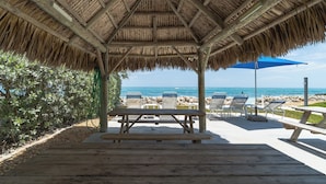 A beachside pavilion with a thatched roof, wooden benches, and lounge chairs. - Key Colony Beach oceanview condo, beach + heated pool (Key Colony Beach)