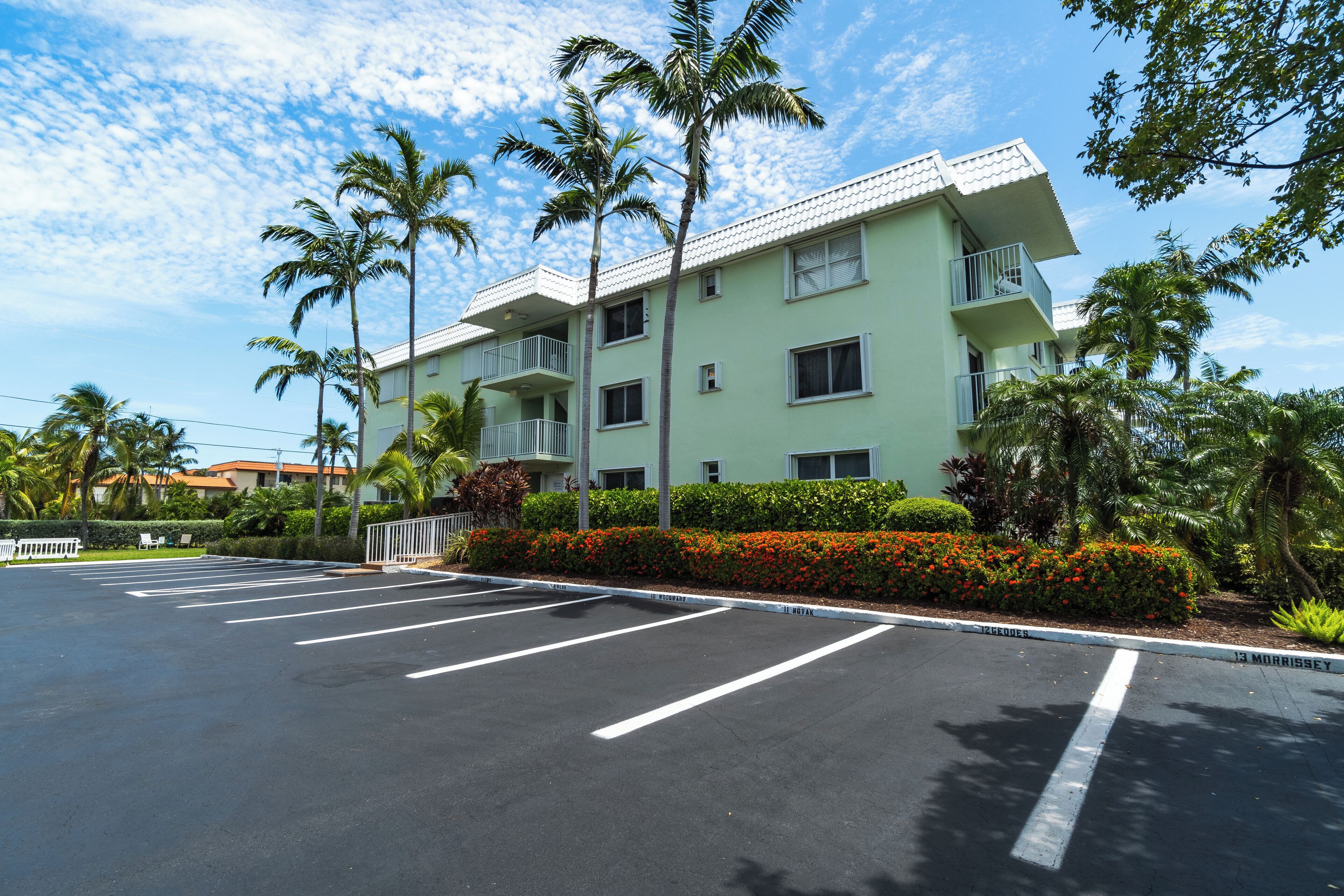 Un hotel su più piani con un parcheggio, circondato da palme e un giardino curato.